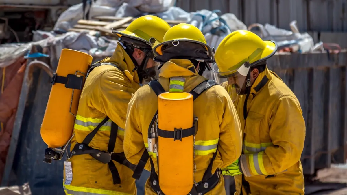 Three firefighters wearing breathing apparatus confer before a deployment