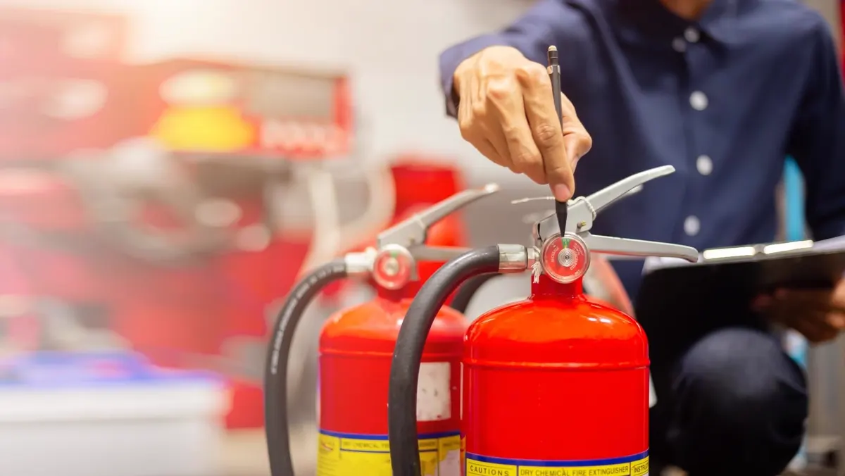 Specialist inspecting fire extinguishers and ticking off a checklist on a clipboard